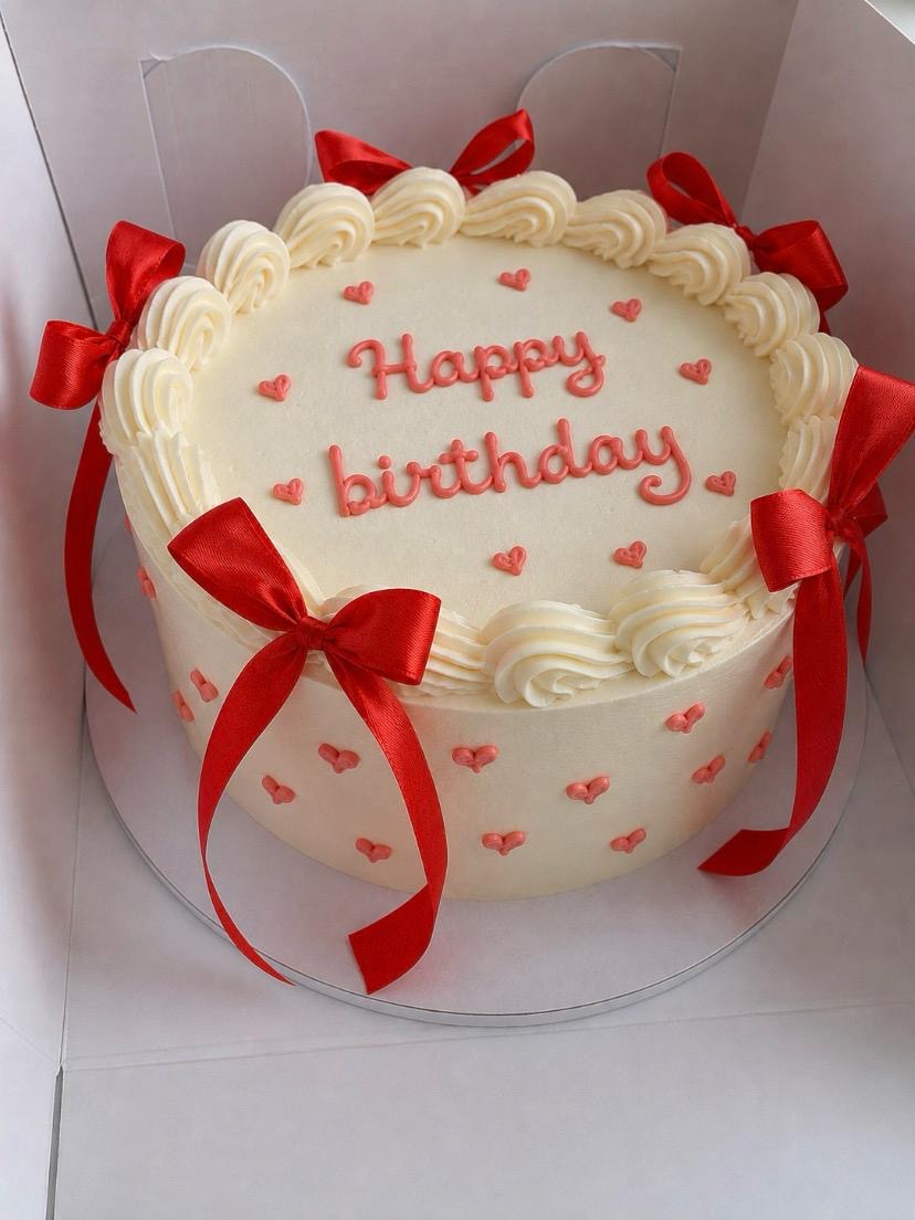 Ivory buttercream birthday cake with red satin bows and piped hearts