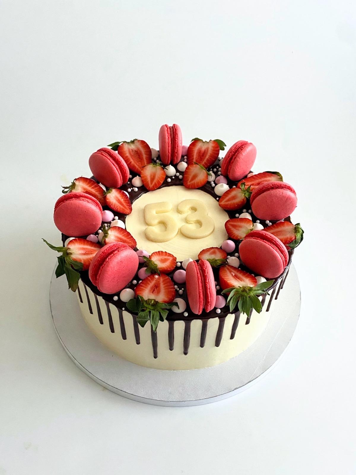 White cake with chocolate drip, fresh strawberries and pink macarons