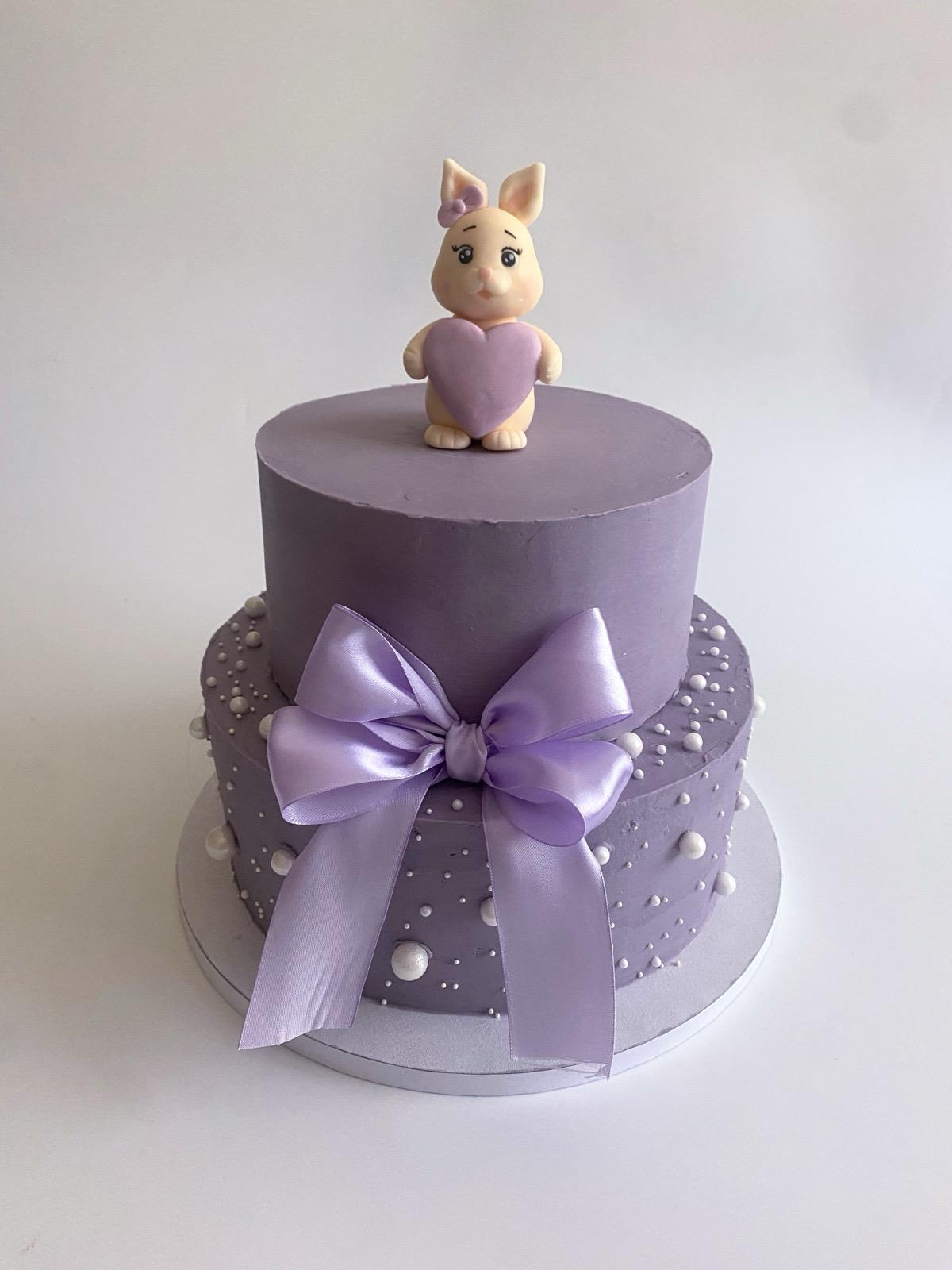 Two-tier lilac cake with sugar pearls, a satin bow and a modelled bunny